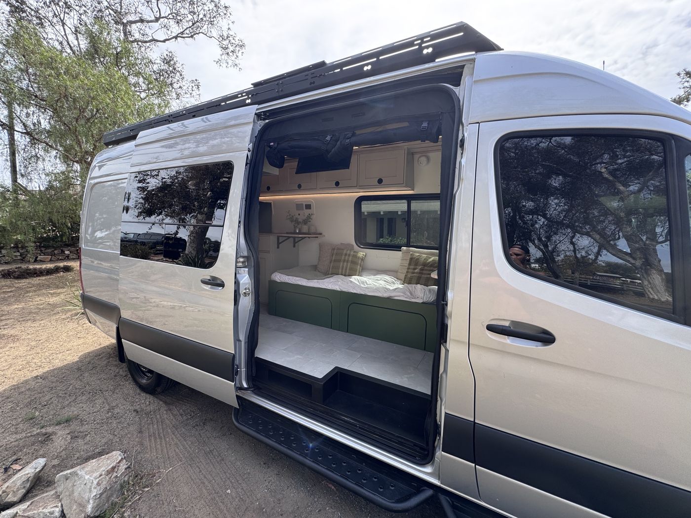 Grove Sprinter with the sliding door open showing the bench bed and olive green cabinet base