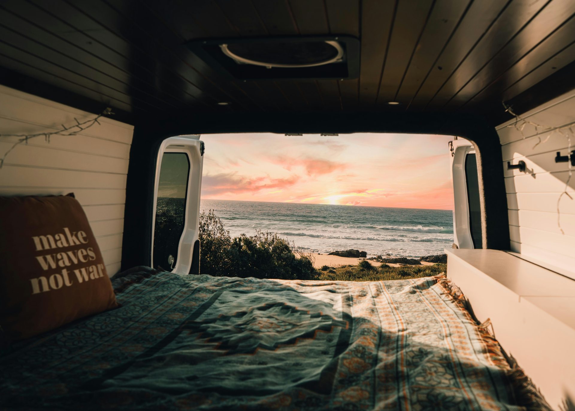 View from the back of a custom van looking out at the ocean at sunset